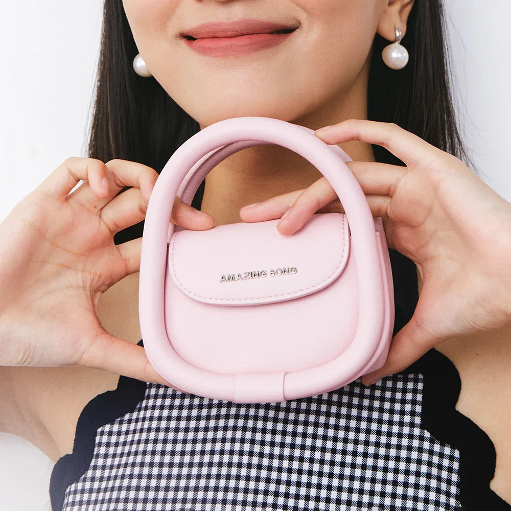 Woman holding a small pink Amazing Song handbag, smiling, against a white background.