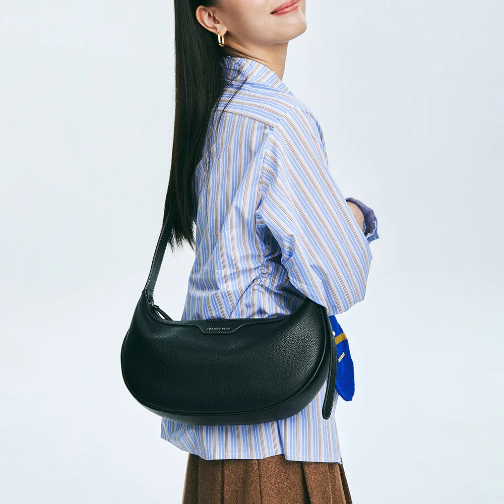 Woman wearing blue striped shirt and brown skirt with black Amazing Song shoulder bag