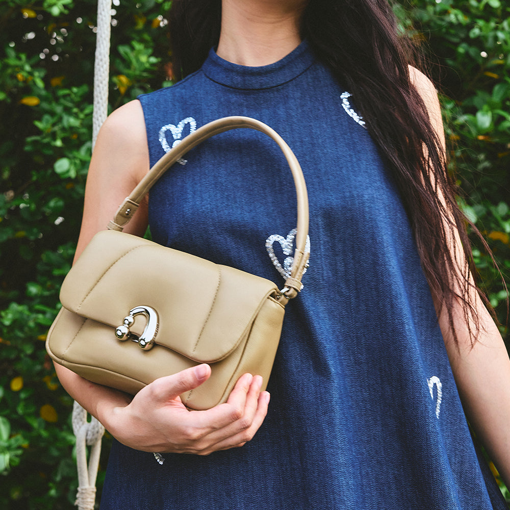 Woman holding tan handbag outdoors, wearing blue dress with heart designs, Amazing Song fashion