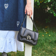 Woman holding black leather shoulder bag, denim dress with heart patches, Amazing Song