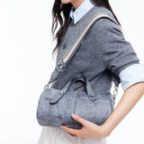 Woman in grey sweater carrying an Amazing Song blue shoulder bag with striped strap.