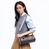 Woman wearing glasses and a grey sweater vest with a stylish brown leather handbag, Amazing Song