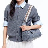 Woman in grey cardigan with light blue shirt holding a stylish grey shoulder bag