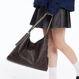 Woman holding large brown leather shoulder bag, wearing black skirt and denim jacket