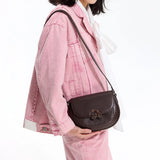 Woman in pink denim jacket with Amazing Song logo, carrying a brown leather shoulder bag