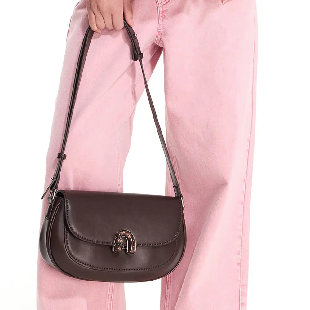 Brown leather shoulder bag with metal clasp, held by a person in pink jeans, Amazing Song