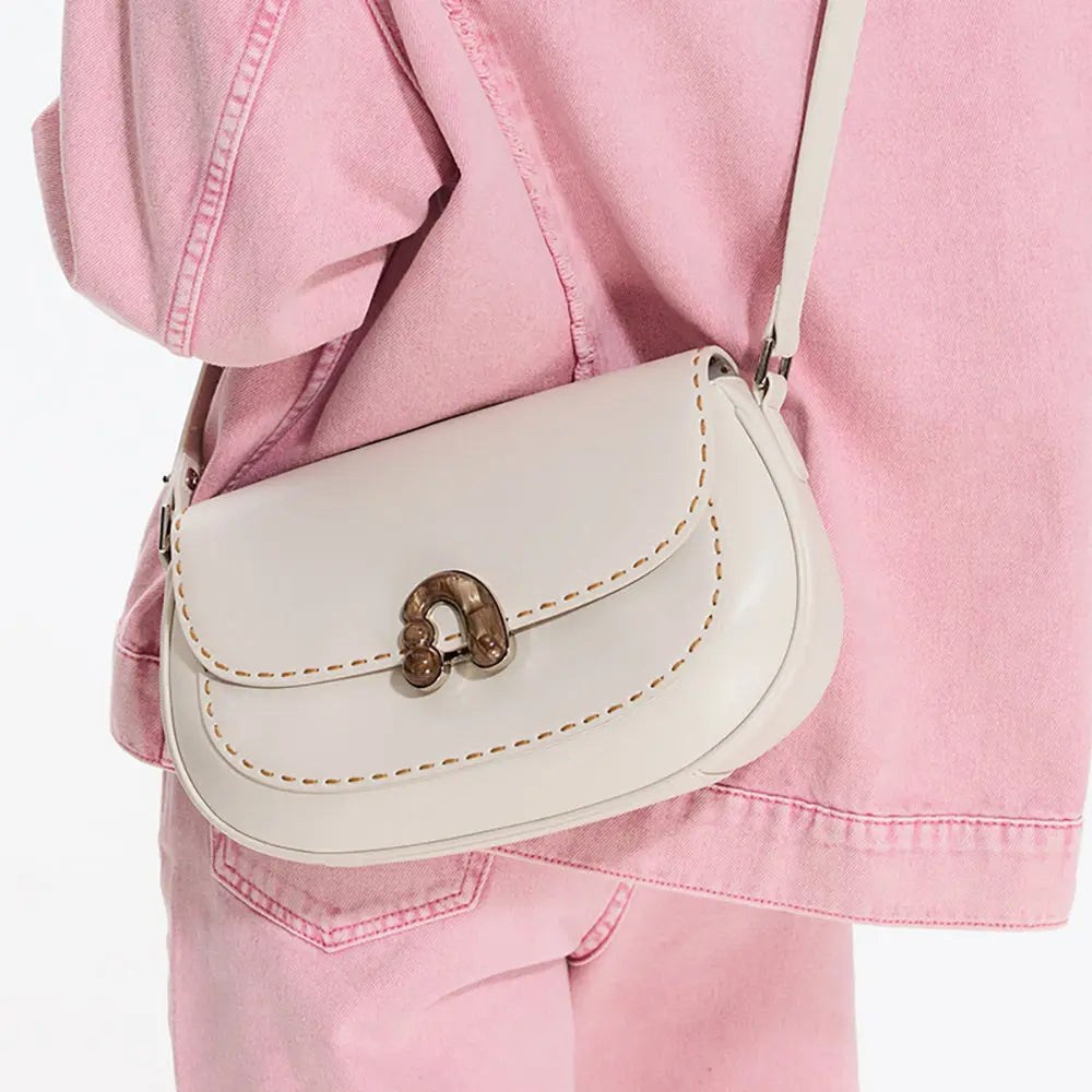 Cream leather shoulder bag with gold clasp, styled over light pink denim jacket and pants