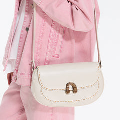 Cream leather crossbody bag with gold clasp, worn over a pink denim jacket and pants