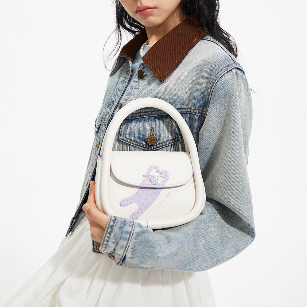 Woman holding Amazing Song white handbag with purple cartoon figure, wearing denim jacket