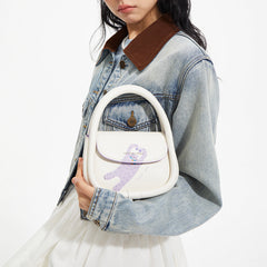 Woman holding Amazing Song white handbag with purple cartoon figure, wearing denim jacket