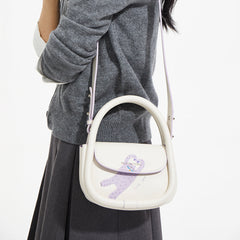 Woman wearing gray sweater and skirt, carrying Amazing Song white shoulder bag with purple bear design