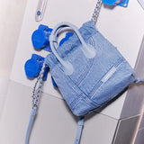 Light blue denim handbag with chain strap, Amazing Song branding, displayed on modern surface
