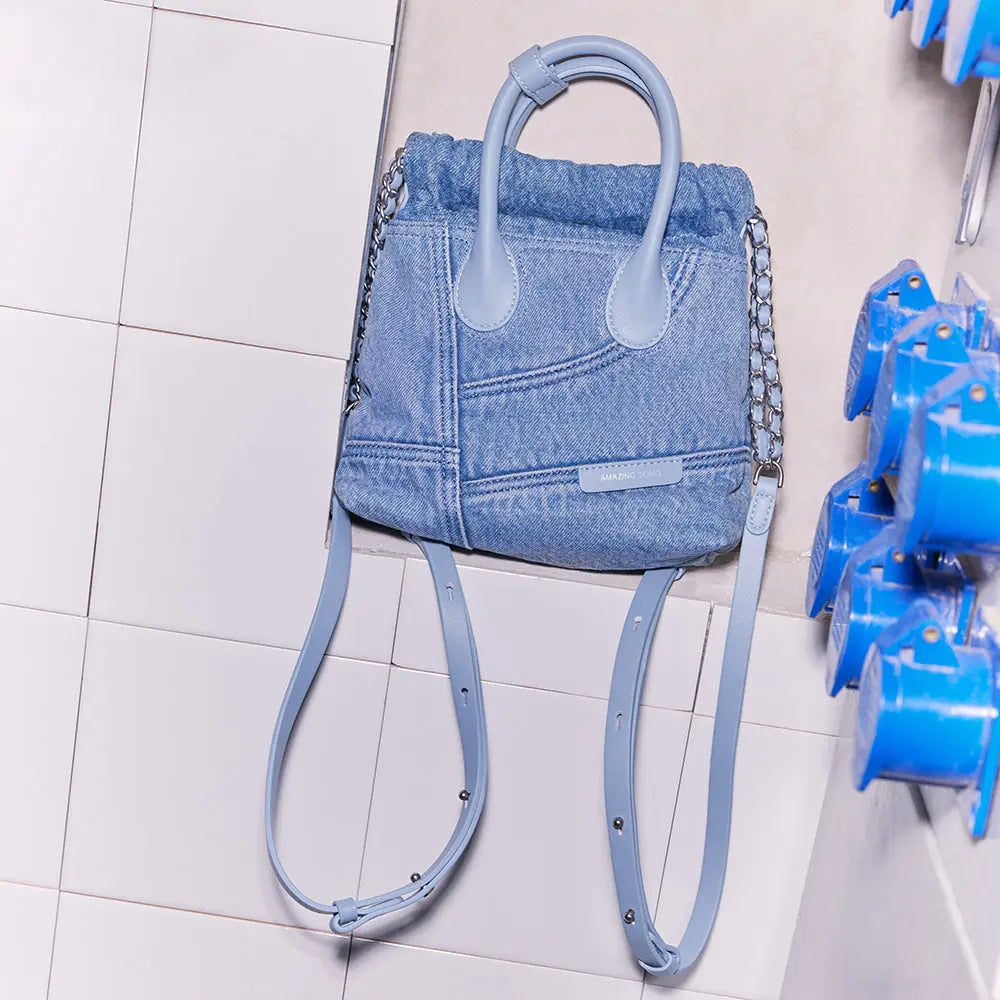 Amazing Song light blue denim backpack with leather straps on white tiled wall