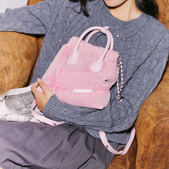 Woman on sofa holding pink Amazing Song bag in cozy outfit, fashion accessory photo