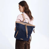 Woman in pink sweater carrying navy denim and tan leather backpack, Amazing Song style.