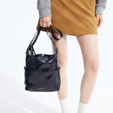 Woman holding black Amazing Song tote bag, brown skirt and grey sweater, white background