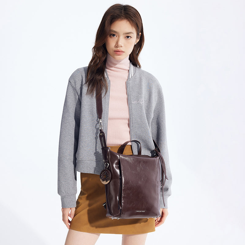 Woman in grey jacket and camel skirt modeling a brown Amazing Song leather bag.