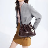 Woman wearing grey jacket and tan skirt with brown Amazing Song bucket bag