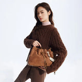 Woman in brown cable-knit sweater holding tan suede bucket bag, Amazing Song fashion