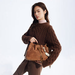 Woman in brown cable-knit sweater holding tan suede bucket bag, Amazing Song fashion