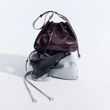 Three Amazing Song leather handbags in burgundy, black, and gray stacked on white background