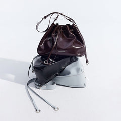 Three Amazing Song leather handbags in burgundy, black, and gray stacked on white background