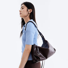 Woman in light blue knit top carrying large black leather Amazing Song shoulder bag