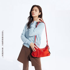 Woman in light blue sweater with brown pants carrying a vibrant red suede shoulder bag