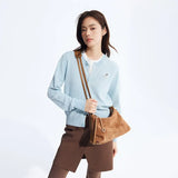 Woman in light blue cardigan with dog embroidery, brown skirt, and tan suede shoulder bag