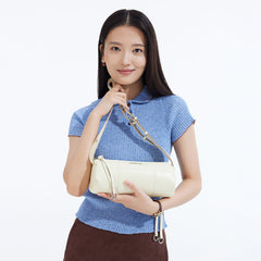 Woman in blue ribbed top holding cream Amazing Song handbag on white background