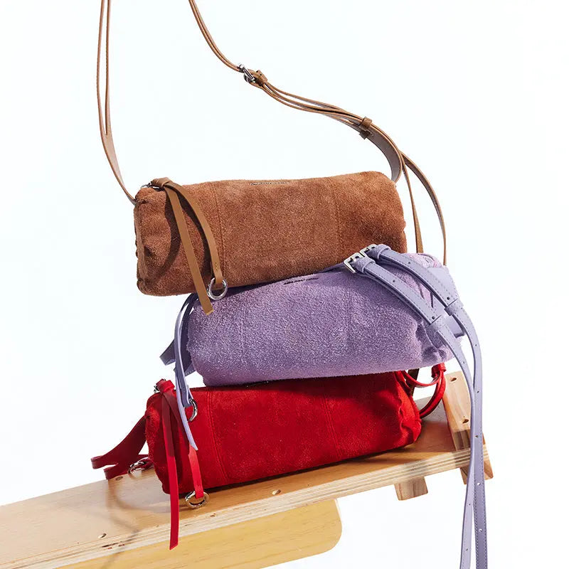 Brown, purple, and red suede shoulder bags stacked on a wooden bench, Amazing Song