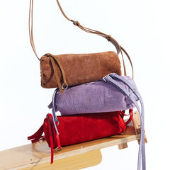 Brown, purple, and red suede shoulder bags stacked on a wooden bench, Amazing Song