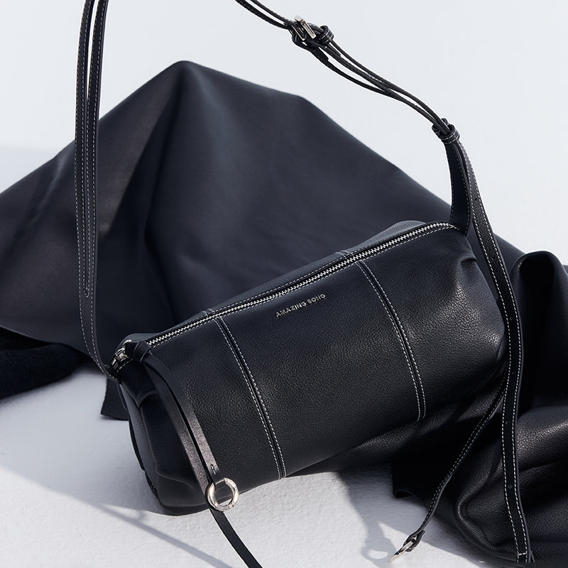 Amazing Song black leather crossbody bag with silver zipper and strap detail on fabric backdrop