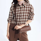 Woman wearing brown plaid shirt and brown skirt, holding a brown leather shoulder bag