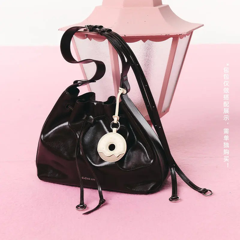 Black Amazing Song bucket bag with donut keychain on pink surface near pink lantern
