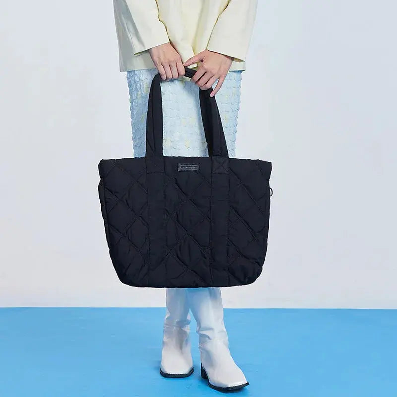 Woman holding large black quilted tote bag, white boots, blue textured skirt, Amazing Song