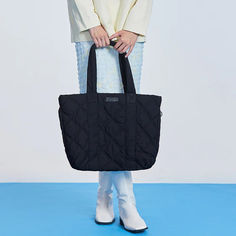 Woman holding large black quilted tote bag, white boots, blue textured skirt, Amazing Song