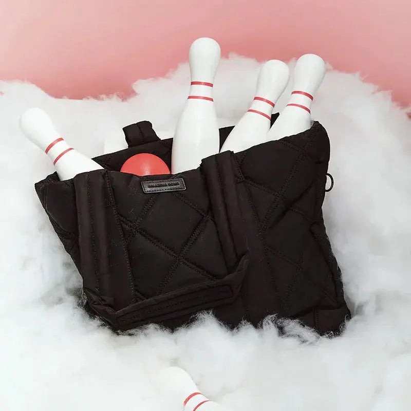 Black quilted Amazing Song bag with bowling pins and red ball on white fluffy surface