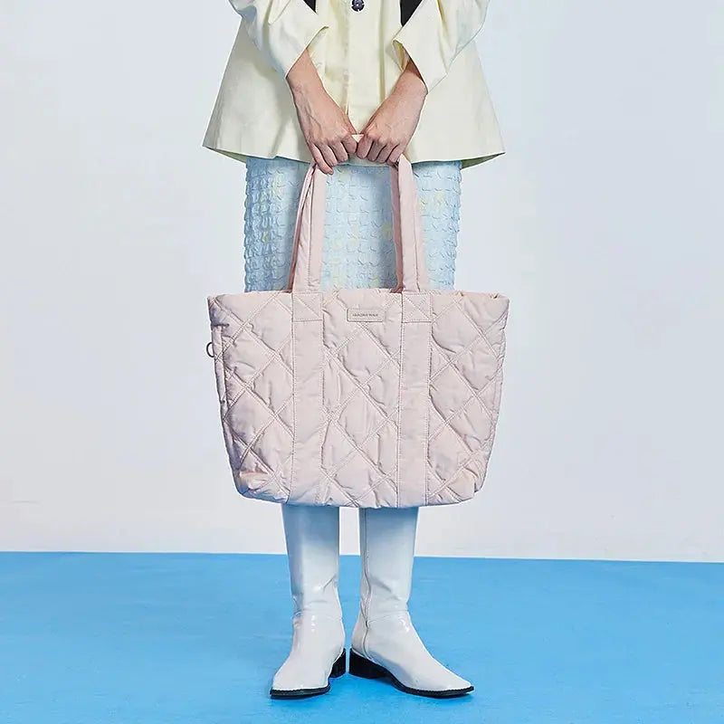Woman holding a large quilted pastel pink tote bag, white boots, blue skirt, Amazing Song