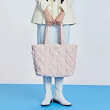 Woman holding a large quilted pastel pink tote bag, white boots, blue skirt, Amazing Song