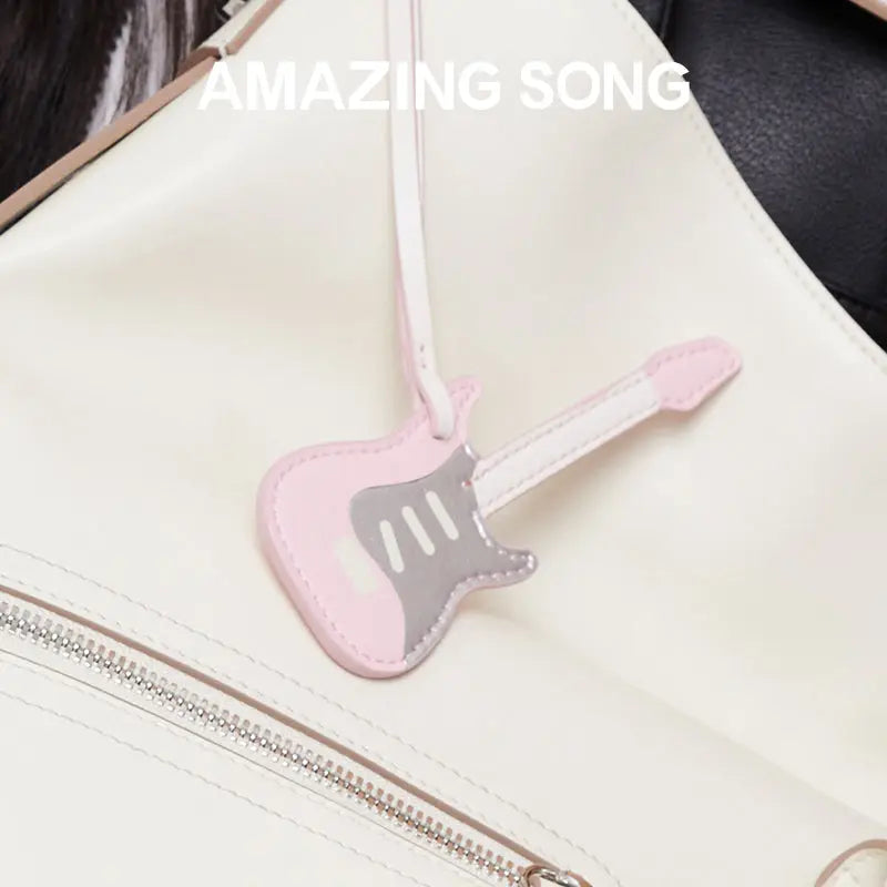 Pink guitar-shaped bag charm on cream backpack, Amazing Song branding visible