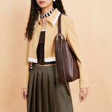 Woman in a beige cropped jacket, pleated skirt, and brown leather shoulder bag, fashion style