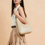 Woman in beige top and skirt posing with a large cream leather shoulder bag, Amazing Song