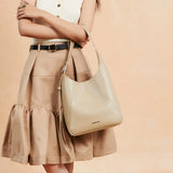 Woman in beige skirt holding a chic beige Amazing Song handbag against neutral background