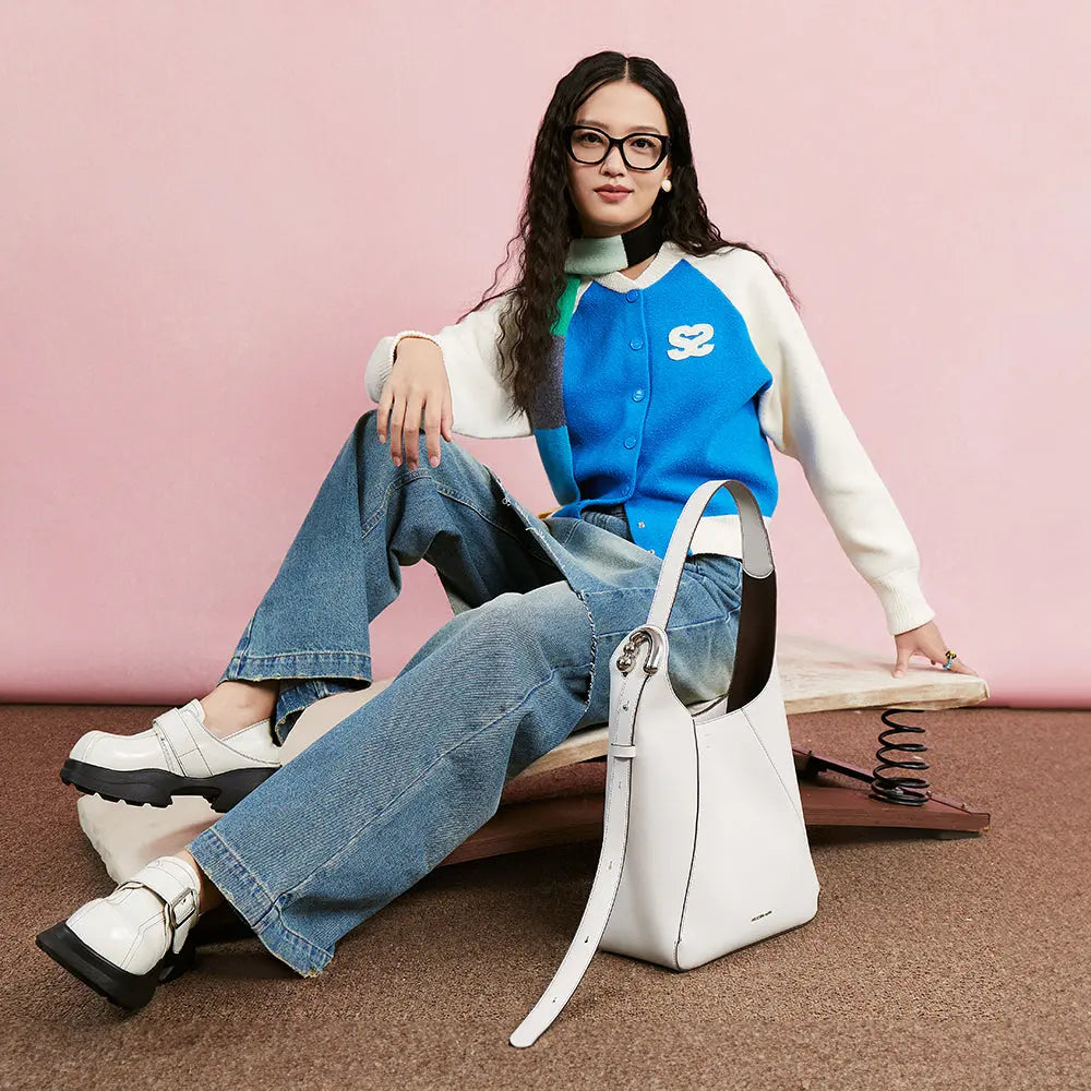 Stylish woman in blue varsity cardigan and jeans with white handbag, Amazing Song fashion