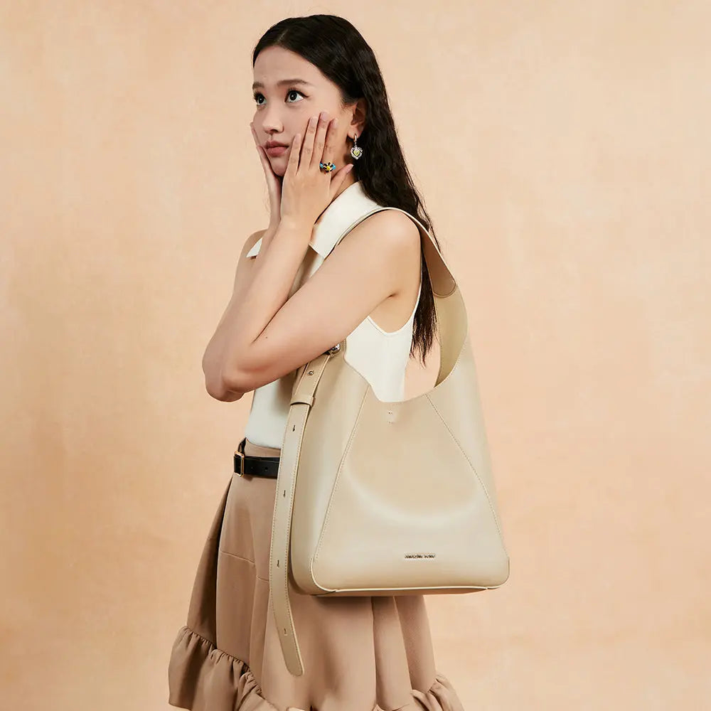 Woman with long hair models a beige shoulder bag against a peach background for Amazing Song