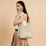 Woman with long hair models a beige shoulder bag against a peach background for Amazing Song
