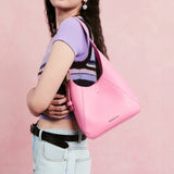 Woman with long hair modeling a pink Amazing Song shoulder bag against a pink background