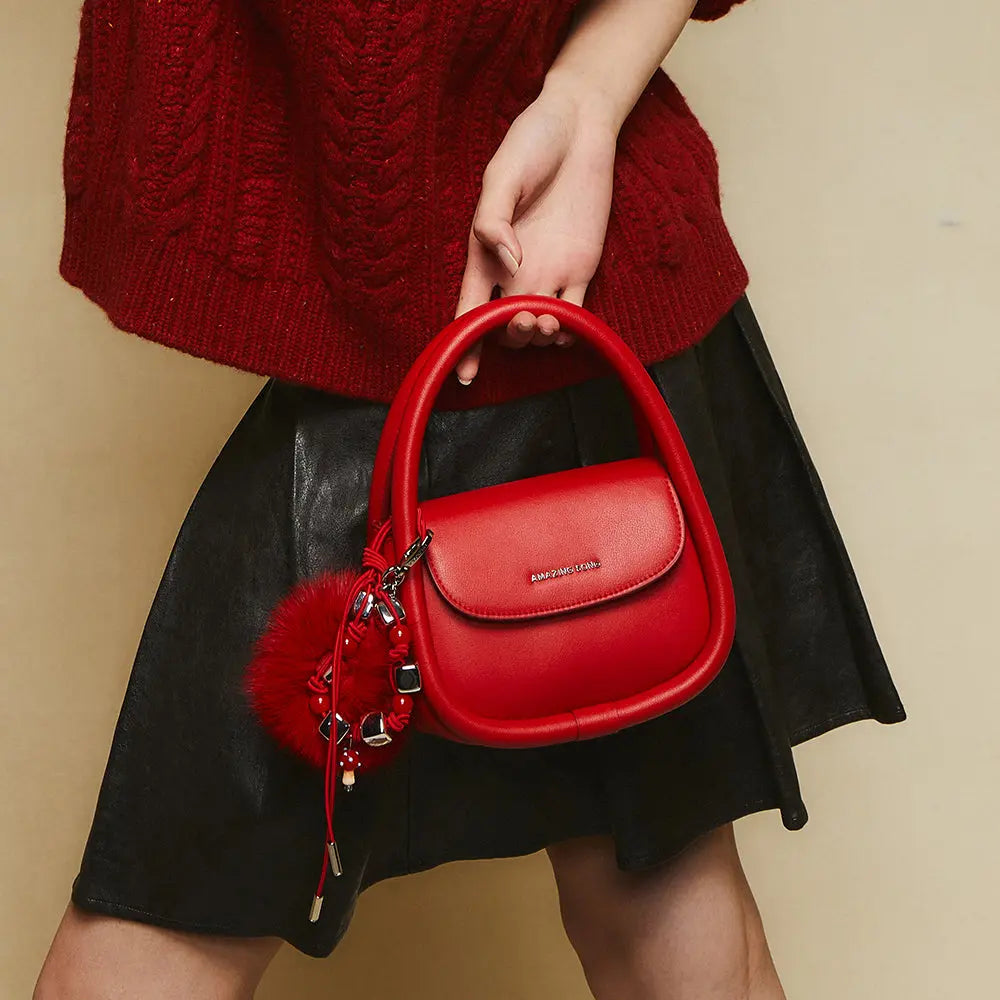 Woman holding red Amazing Song handbag with charm, wearing red sweater and black skirt