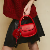 Woman holding red Amazing Song handbag with charm, wearing red sweater and black skirt